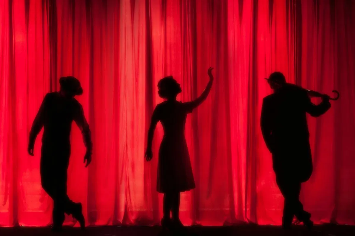 Performers silhouetted against a red stage curtain